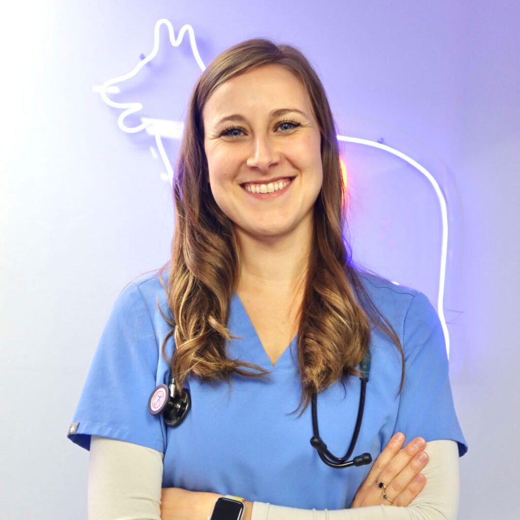 smiling female veterinarian with arms crossed standing in front of neon dog wall decoration